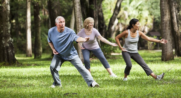 man and two women doing tai chi in a park